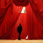 Un homme se tient devant une installation artistique composée de grands rideaux rouges rappelant ceux d’un théâtre.