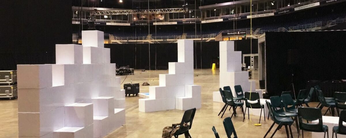 Grande salle sombre en cours d’installation pour un workshop, avec des cloisons blanches en cubes Tetrix au premier plan.