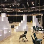 Grande salle sombre en cours d’installation pour un workshop, avec des cloisons blanches en cubes Tetrix au premier plan.