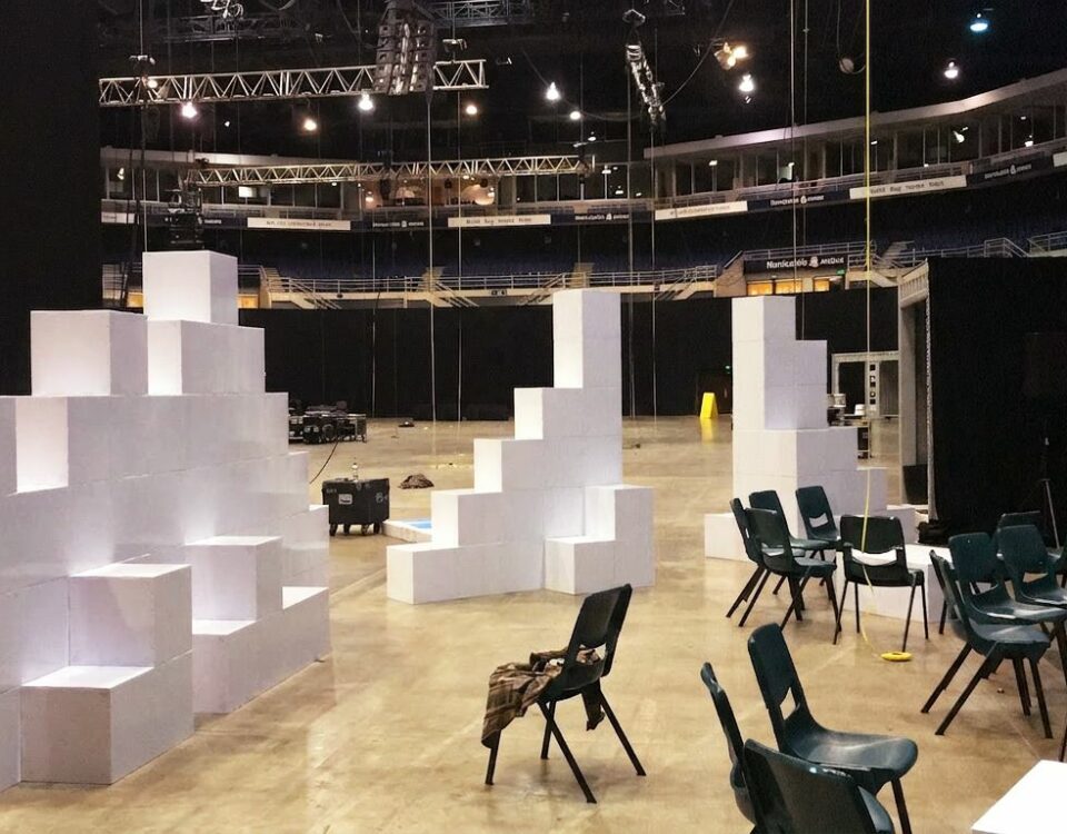 Grande salle sombre en cours d’installation pour un workshop, avec des cloisons blanches en cubes Tetrix au premier plan.