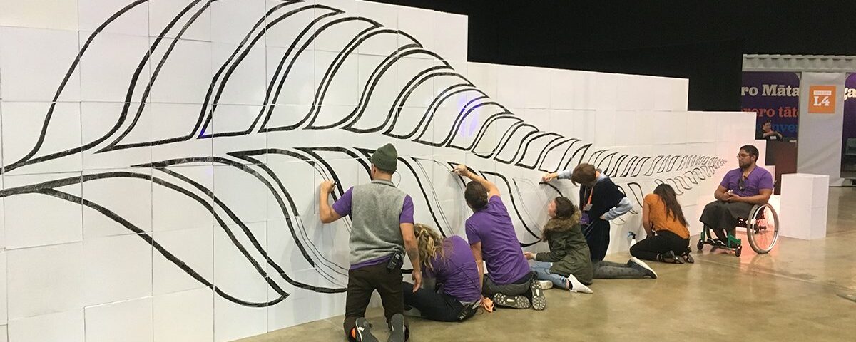 Équipe réalisant un scribing sur un mur Velleda de 10 mètres composé de cubes Tetrix, dessinant une feuille de fougère symbole de la Nouvelle-Zélande