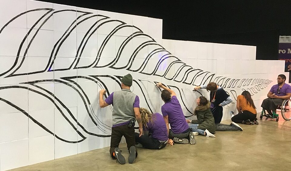 Équipe réalisant un scribing sur un mur Velleda de 10 mètres composé de cubes Tetrix, dessinant une feuille de fougère symbole de la Nouvelle-Zélande