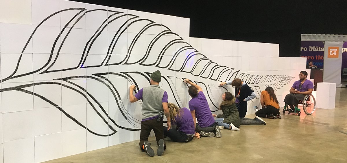 Équipe réalisant un scribing sur un mur Velleda de 10 mètres composé de cubes Tetrix, dessinant une feuille de fougère symbole de la Nouvelle-Zélande