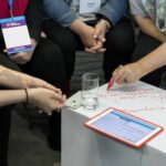 Participants en atelier collaboratif assis autour d’une table modulaire Tetrix recouverte de panneaux Velleda, prenant des notes directement sur la surface de travail.